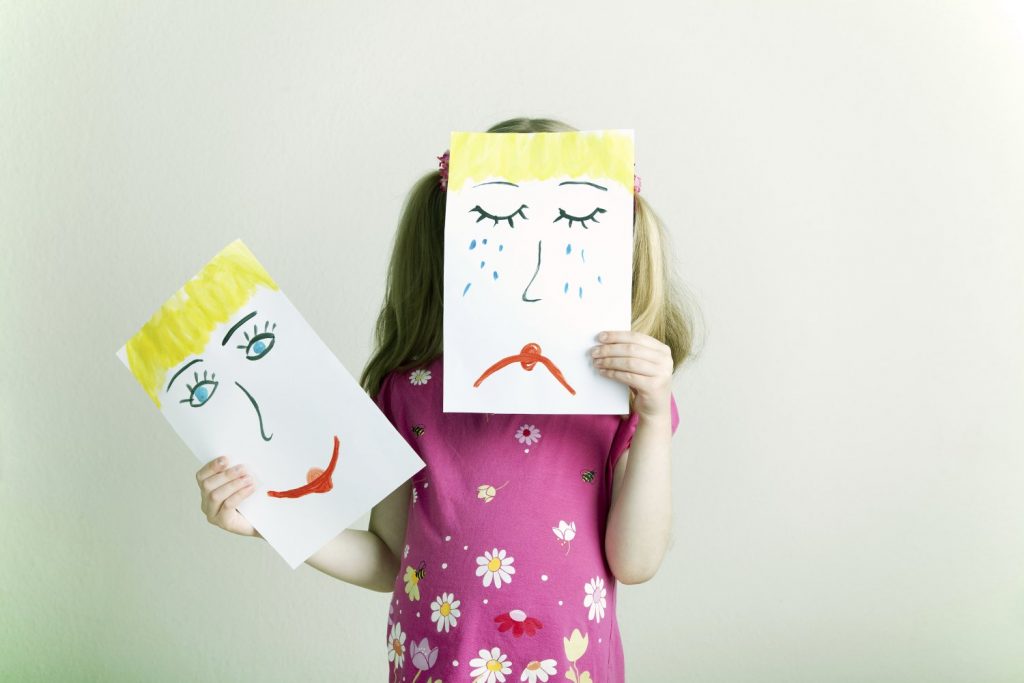 Little girl using picture of a sad face to cover her own