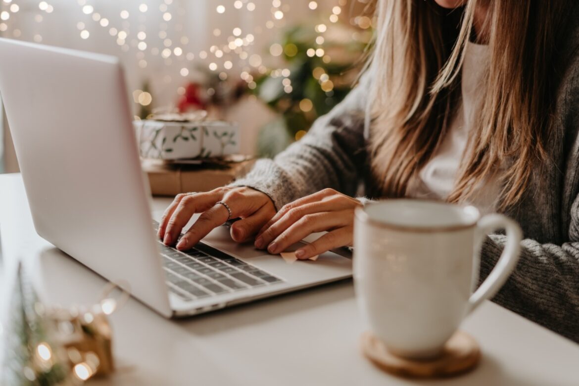 woman with long hair typing on laptop with christmas mug next to her
